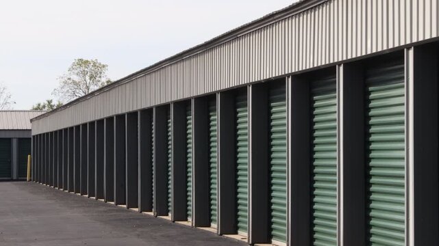Zoomed in tilting down view of a row of green storage unit doors with fall leaves on the ground and a slight shake from the heatwave coming off the asphalt.