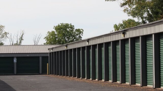 Zoomed in view of a row of green storage unit doors with fall leaves on the ground and a slight shake from the heatwave coming off the asphalt.