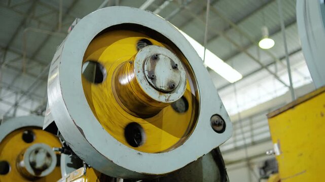 Close-up of heavy industrial stamping machine flywheel rotating inside a manufacturing factory. Mechanical engineering production equipment operating inside a modern metal processing facility.