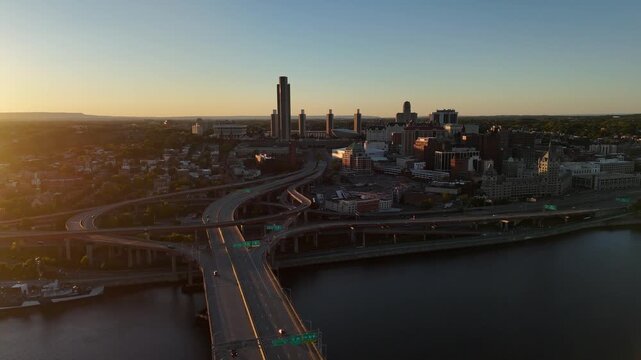 Albany New York downtown skyline and highway interchange spanning the Hudson River during golden hour sunset 4k aerial drone video