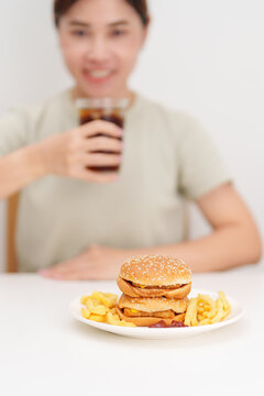 woman eating Juicy beef burger with melted cheddar cheese, potato chips and carbonated Soft drinks. Unhealthy, High calorie, Fast food craving, Obesity, diet, weight loss, junk food and lifestyle