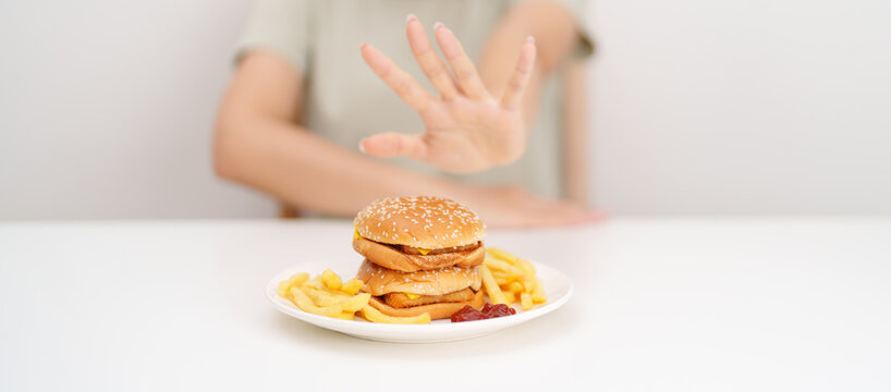 Unhappy woman showing Rejecting and refusing with Juicy beef burger, potato chips and carbonated Soft drinks. Unhealthy, High calorie, Fast food craving, Obesity, diet, weight loss and junk food