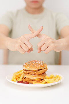 Unhappy woman showing Rejecting and refusing with Juicy beef burger, potato chips and carbonated Soft drinks. Unhealthy, High calorie, Fast food craving, Obesity, diet, weight loss and junk food