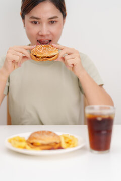 woman eating Juicy beef burger with melted cheddar cheese, potato chips and carbonated Soft drinks. Unhealthy, High calorie, Fast food craving, Obesity, diet, weight loss, junk food and lifestyle