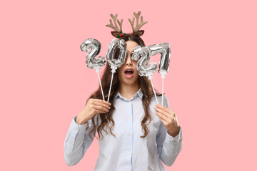 New year celebration and holiday excitement, young woman holding 2021 silver balloons over eyes with reindeer antlers headband on pink background © Pixel-Shot