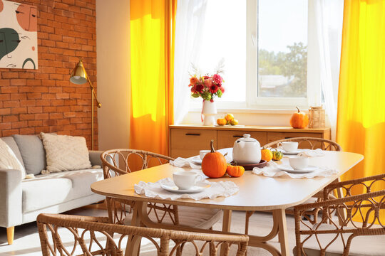 Autumn home interior, cozy dining room with pumpkin decor and tea set for seasonal celebration and thanksgiving gathering in a bright modern apartment
