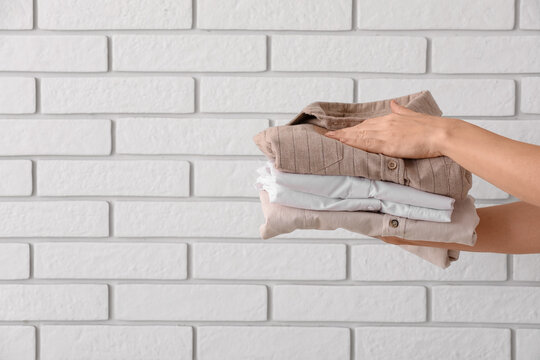 Household chores and laundry organization, person holding a stack of clean folded shirts against a white brick wall for home maintenance