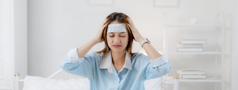 Woman feeling sick holding head with cooling patch on forehead. Healthcare lifestyle image showing headache, fever, flu symptoms, illness, stress, fatigue and recovery.