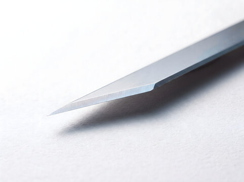 A sharp and precise exacto blade lying on a clean white paper surface, highlighting industrial craft design