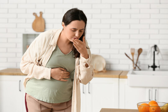 Morning sickness and pregnancy nausea, pregnant woman feeling unwell with stomach pain and vomiting in a home kitchen during the first trimester