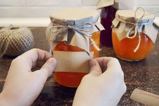 Hands applying blank brown label onto jar of homemade jam