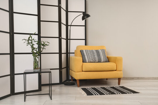 Interior design and home comfort, yellow armchair with patterned pillow and floor lamp in modern living room with bamboo plant and folding screen