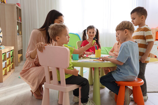 Early childhood education and preschool learning, teacher helping diverse group of children with drawing and creative activities in a bright classroom