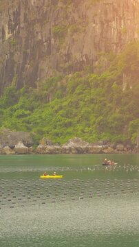 Tourists kayaking through an oyster pearl farm and lush green limestone mountain in Ha Long Bay, Vietnam