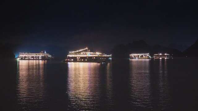 Night view of illuminated cruise ships anchored in Ha Long Bay, Vietnam, at dusk with dramatic sunset clouds and limestone karsts