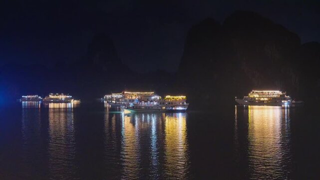 Night view of illuminated cruise ships anchored in Ha Long Bay, Vietnam, at dusk with dramatic sunset clouds and limestone karsts