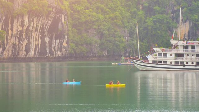 Tourists kayaking through an oyster pearl farm and lush green limestone mountain in Ha Long Bay, Vietnam
