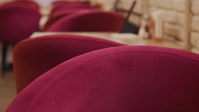 Close up of hand gently touching backrest of red velvet chairs in soft lighting. scene shows multiple identical maroon upholstered seats arranged neatly with tables and condiment holders