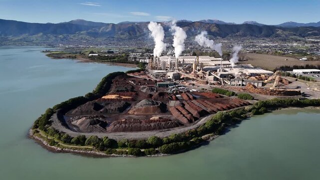 Richmond, Tasman region, New Zealand - 11 September 2026: Aerial view of the Nelson Pine factory with industrial smoke stacks and wood chip piles by the water.