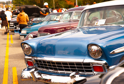 Classic blue vintage car parked at a sunny outdoor street exhibition showcasing retro automotive design, polished chrome bumper details, bright headlights, and a vibrant crowd of car enthusiasts