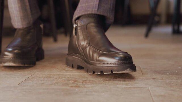 Close up of man brown leather ankle boot with side zipper and thick sole on wooden floor. Boot material texture detail visible soft lighting in indoor setting with blurred background