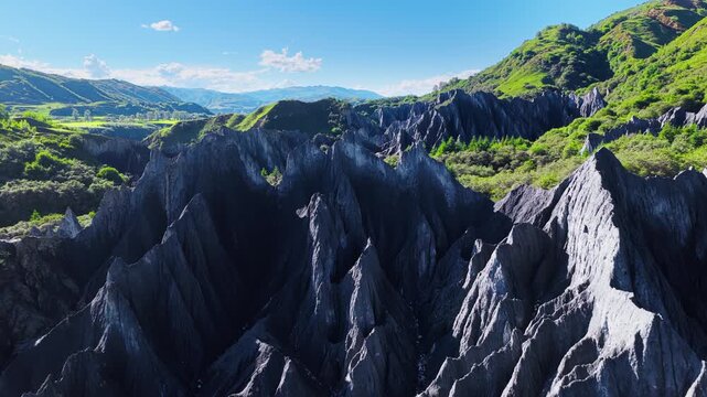Jagged black rock formations rise dramatically under a clear blue sky, surrounded by lush green hills in Sichuan province.