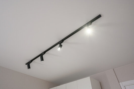 Black track lighting system with cylindrical spotlights, white ceiling. beige walls, minimalist interior, sleek design. adjustable spotlights. modern fixture. ceiling mount