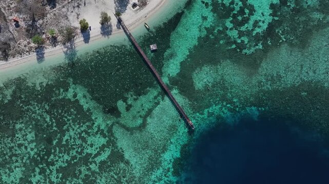 Kecamatan Komodo, Indonesia - 09 September 2026: Aerial view of Kanawa Island with its long wooden pier extending into the turquoise coral reef waters.
