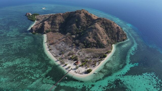 Kecamatan Komodo, Indonesia - 09 September 2026: Aerial view of Kanawa Island with its pristine white sand beach, turquoise coral reefs, and rugged hills surrounded by the Flores Sea.