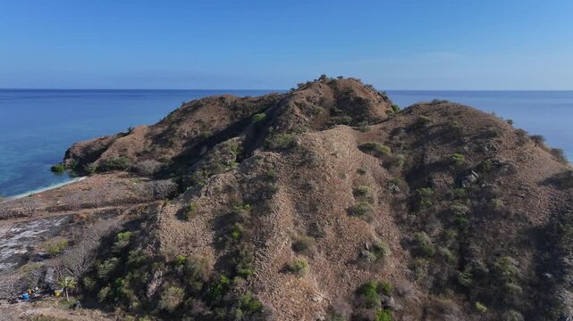 Kecamatan Komodo, Indonesia - 09 September 2026: Aerial view of Kanawa Island with its dry, rugged hills and clear blue sea under a bright sky.