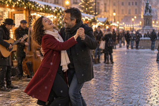 Happy couple dancing to street musicians at festive christmas market on snowy evening in old town square