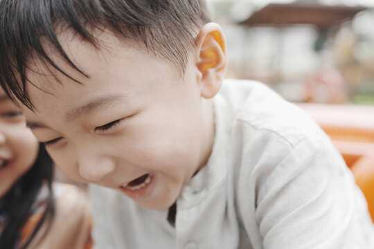 Childhood happiness and joyful laughter concept, close up of cute Asian boy laughing with squinting eyes during outdoor fun, representing kid excitement, carefree play, and positive emotion.