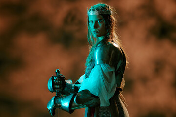 Obraz premium Portrait of young adult Caucasian woman wearing armor and crown holding sword representing leadership and power. Visual concept suitable for historical marketing