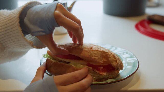 Close up of person assembling food on plate placing top bread slice onto vegetables and meat in open sandwich. scene includes visible kitchen elements like teapot countertop objects