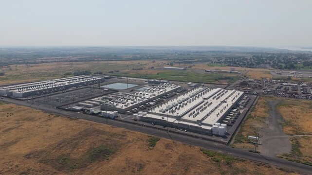 Large Web Services data center with industrial buildings, cooling units, electrical substations, and arid landscape, drone orbit.