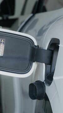Close up shot of hand plugging power charger into white electric vehicle charging port at home.