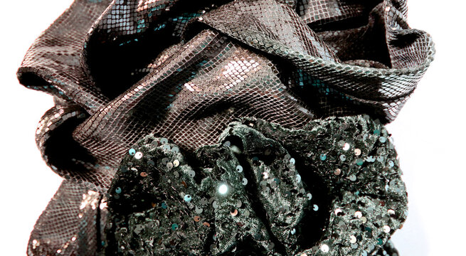 A crumpled piece of fabric shows various textures and shades. The fabric includes shiny sequins and smooth patterns. Light reflects off the surface.