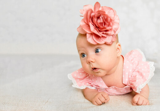 Baby girl 5-6 months old in pink dress and flower headband lies on tummy at home, dressed up vertical portrait