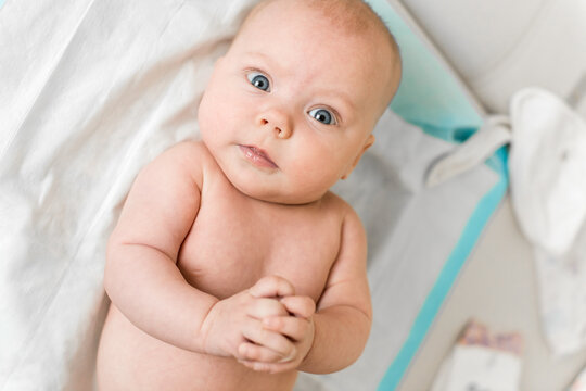 Baby 5-6 months old lies on back on a changing surface at home and looks at camera during everyday care