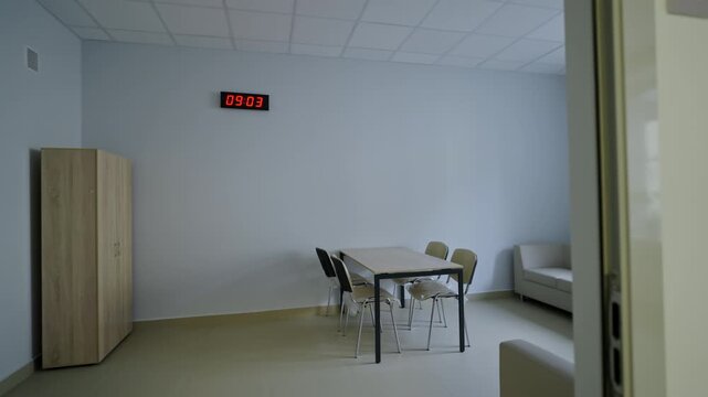 Simple modern interior features plain walls and flooring. Quiet atmosphere suggests morning office setting. Digital clock displays time