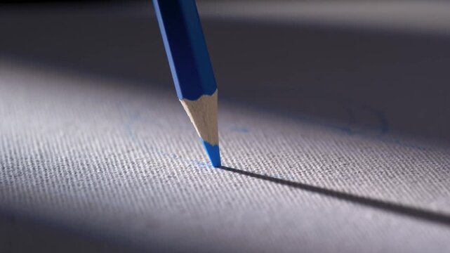 Macro shot of drawing lines with a blue colored pencil on textured paper