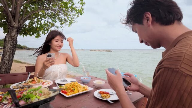 Asian Couple Using Smartphones at Seaside Restaurant Table During Lunch Date