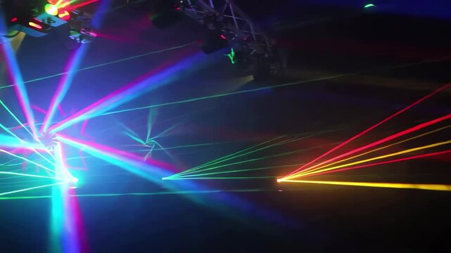 Slow pan over vibrant laser light beams weaving intricate abstract patterns in a dark environment, creating a mesmerizing visual experience that captivates the viewer