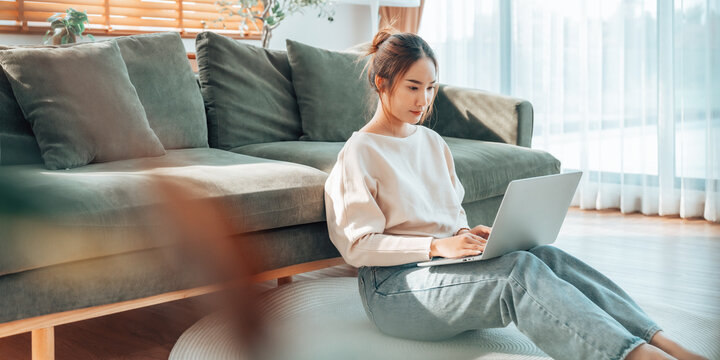 Young Asian woman working from home. Freelancer businesswoman using laptop at sunny room. Student female learning and working at home