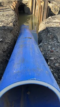 Polyethylene sewage pipe of large diameter in the excavated trench with soil layers, sheet pile shoring and sewer manhole visible