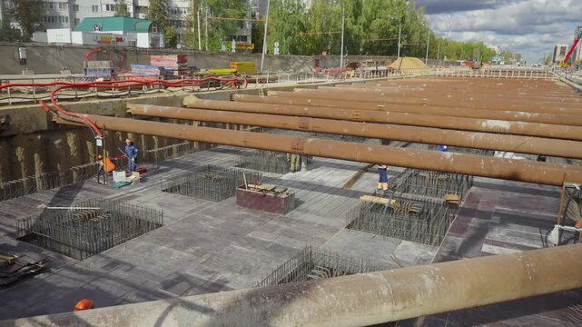 Deep excavation pit shows foundation work in progress on urban construction site. Large brown pipes support walls around construction area.