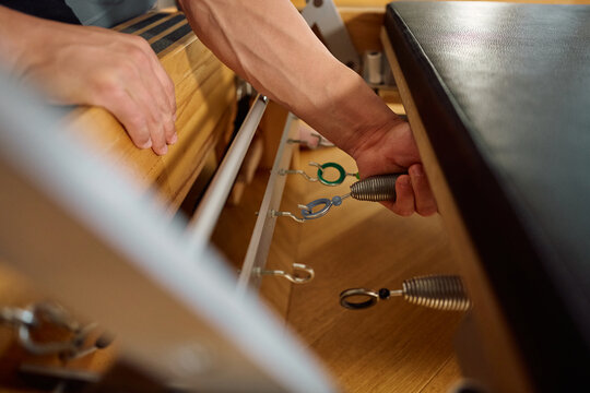 Close up of man adjusting resistance spring on Pilates reformer machine.