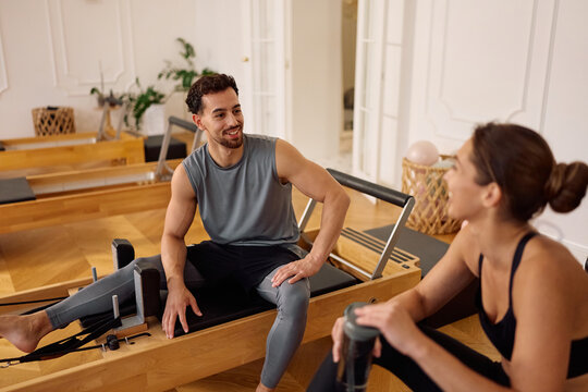 Athletic man talking to female friend while working out on Pilates reformer in health club.