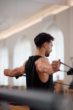 Athletic man doing upper body exercise with resistance straps during Pilates training.