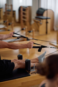 Close up of athlete pulling resistance straps while practicing on Pilates reformer machine.
